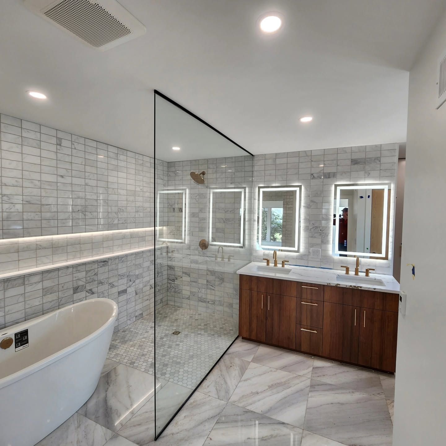 Modern bathroom with freestanding tub, glass shower wall, wood vanity, and marble tile accents