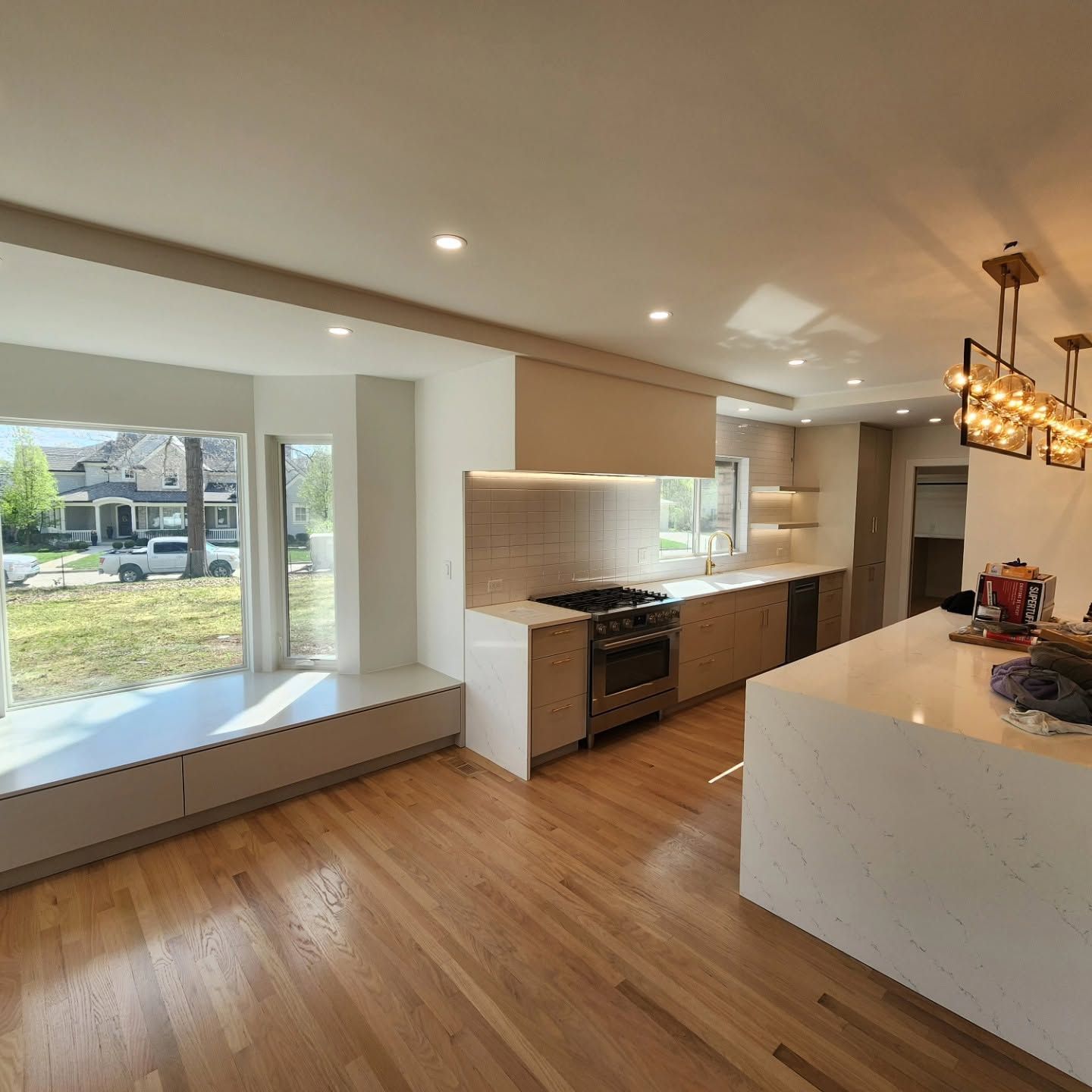 Bright modern kitchen with wood floors, white cabinets, island, and large window seat overlooking a yard