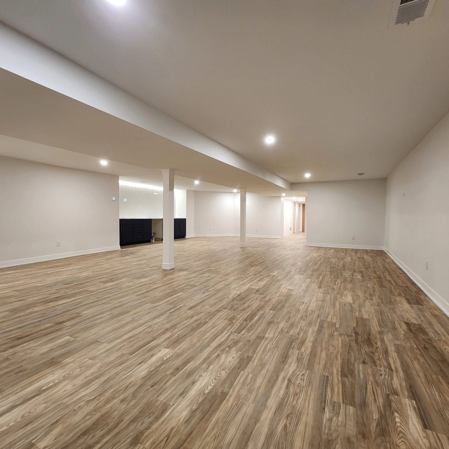 Spacious empty room with wood-look flooring, white walls, recessed lights, and a columned open layout.