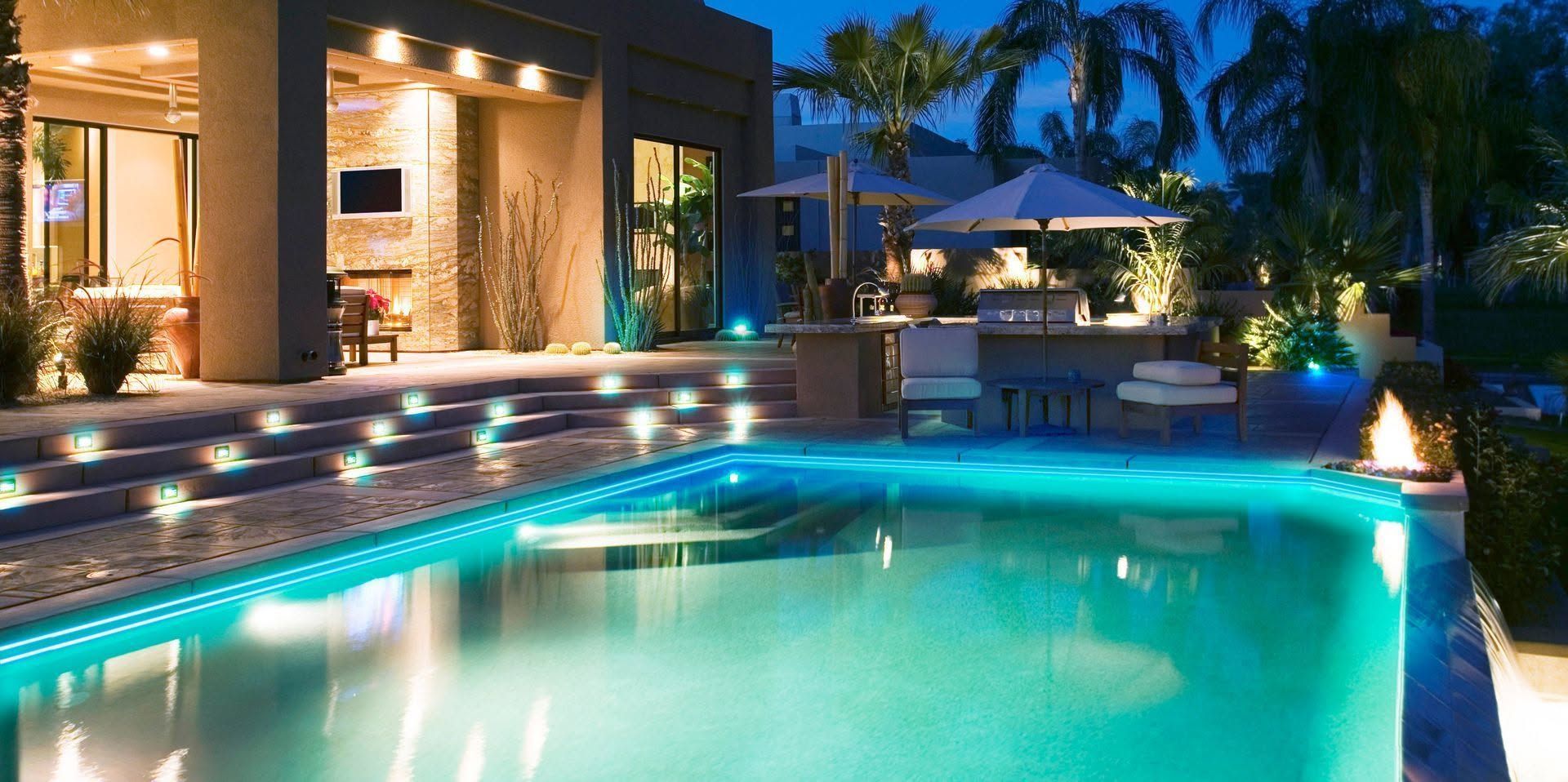 Luxury backyard pool lit at dusk beside a modern home and palm trees