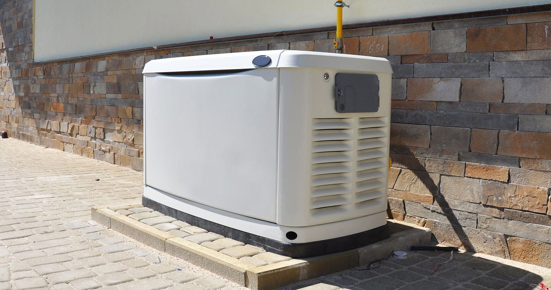 White portable generator on wooden base beside a stone building in bright sunlight