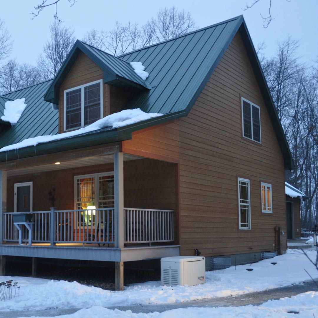 Snowy two-story brown house with a front porch and metal roof at dusk