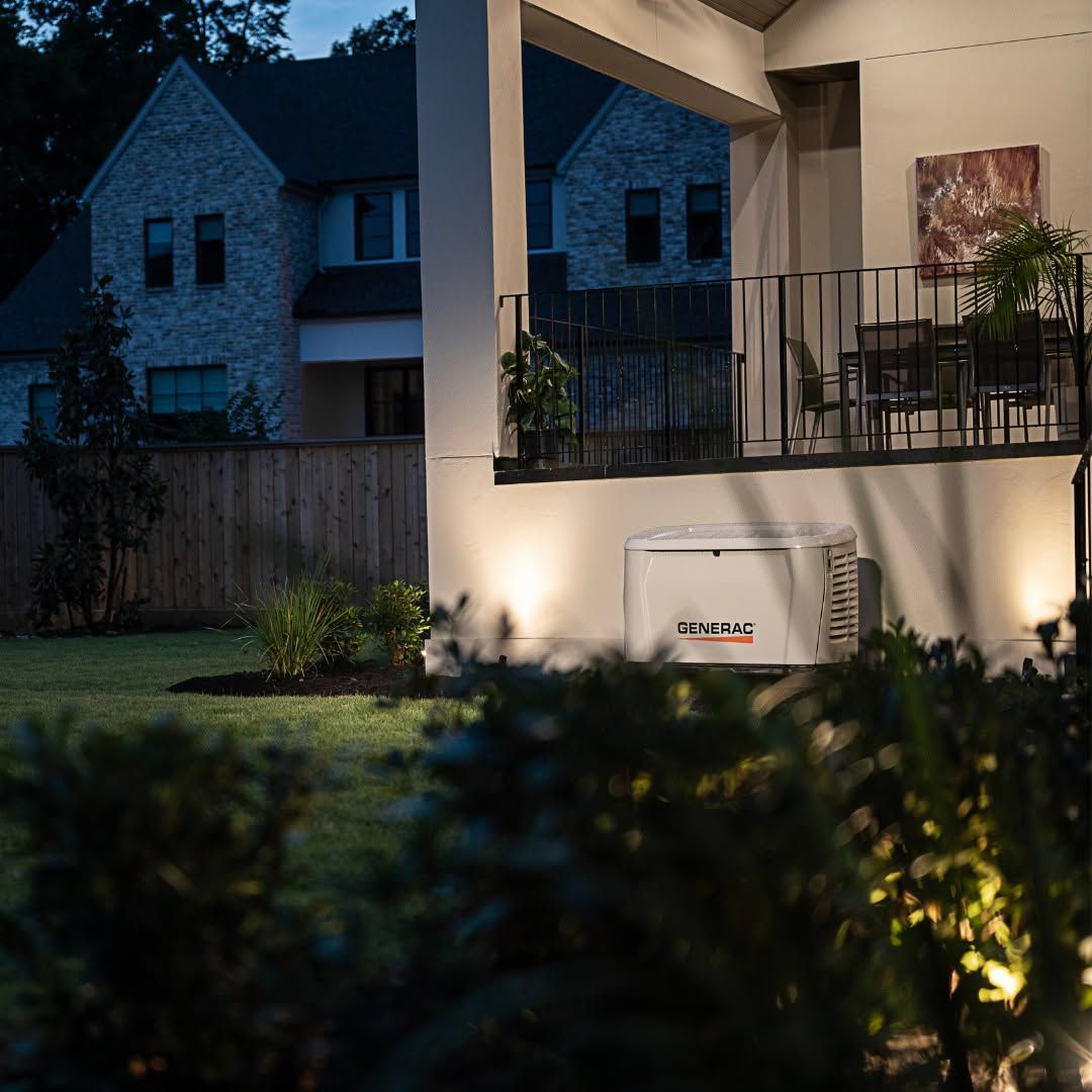 Nighttime view of a house porch with warm lights, balcony railing, and a lit yard in the foreground