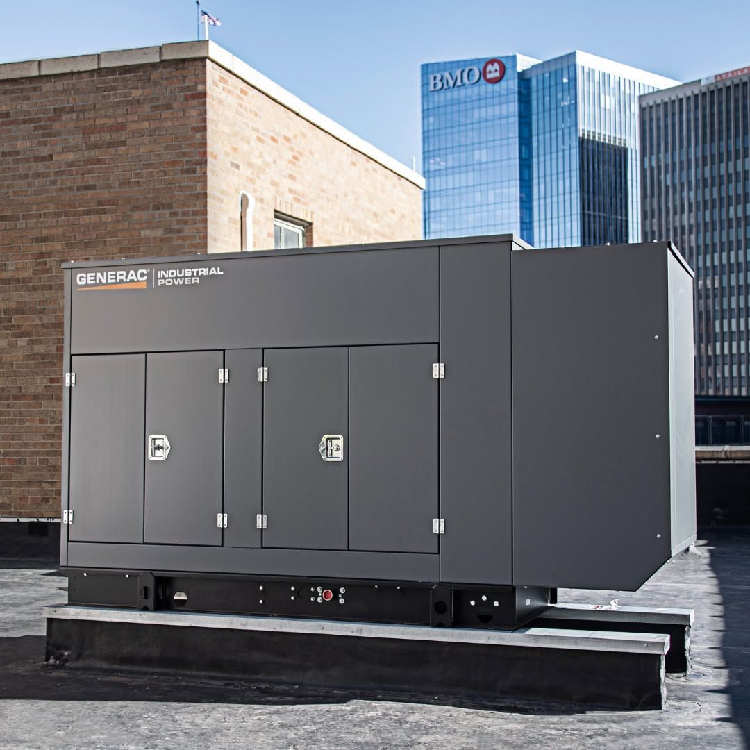 Large gray rooftop generator unit with double doors on a city rooftop, with buildings in the background