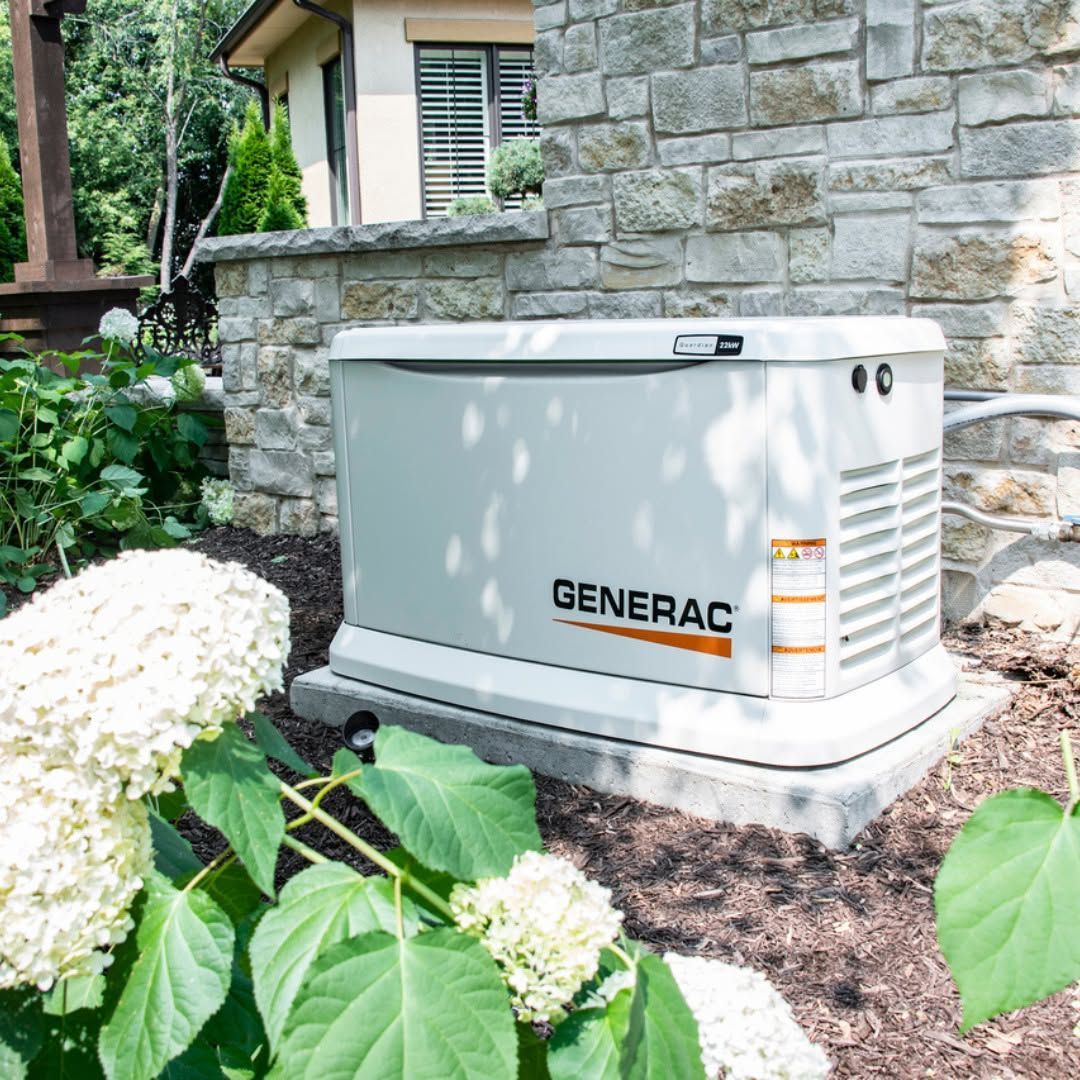 Generac home standby generator beside a stone house, surrounded by mulch and greenery