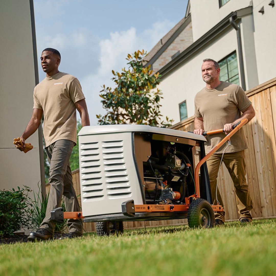 Two workers move a portable generator beside a house on a grassy lawn.