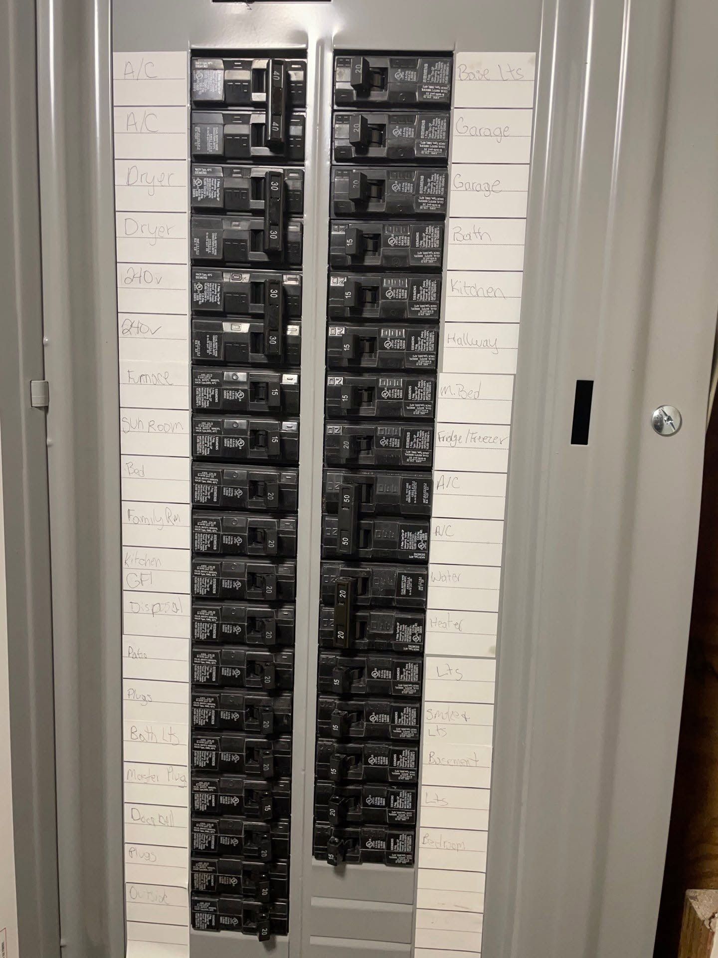 Electrical breaker panel with many labeled circuit breakers in a white closet.