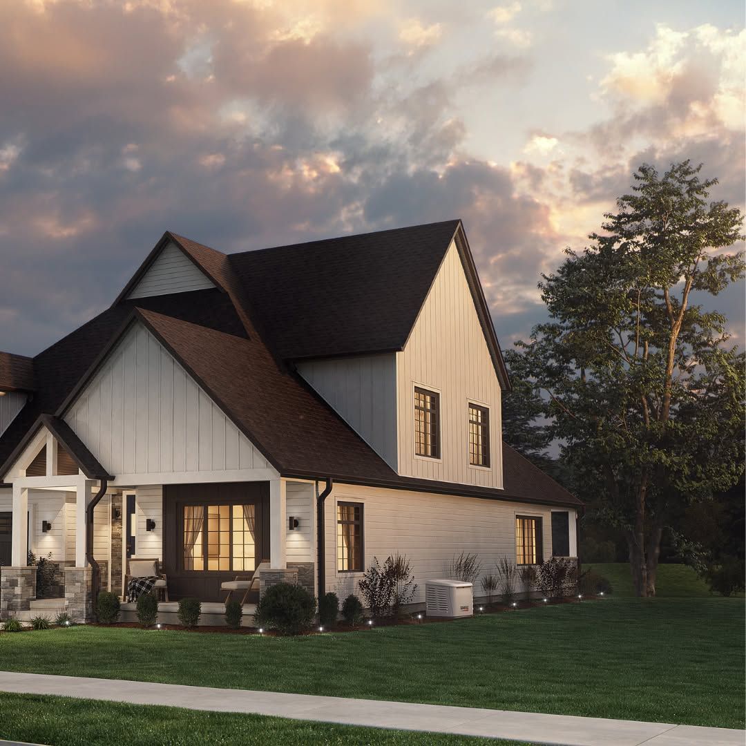 Modern two-story farmhouse at dusk with a dark roof, lit windows, lawn, and a large tree