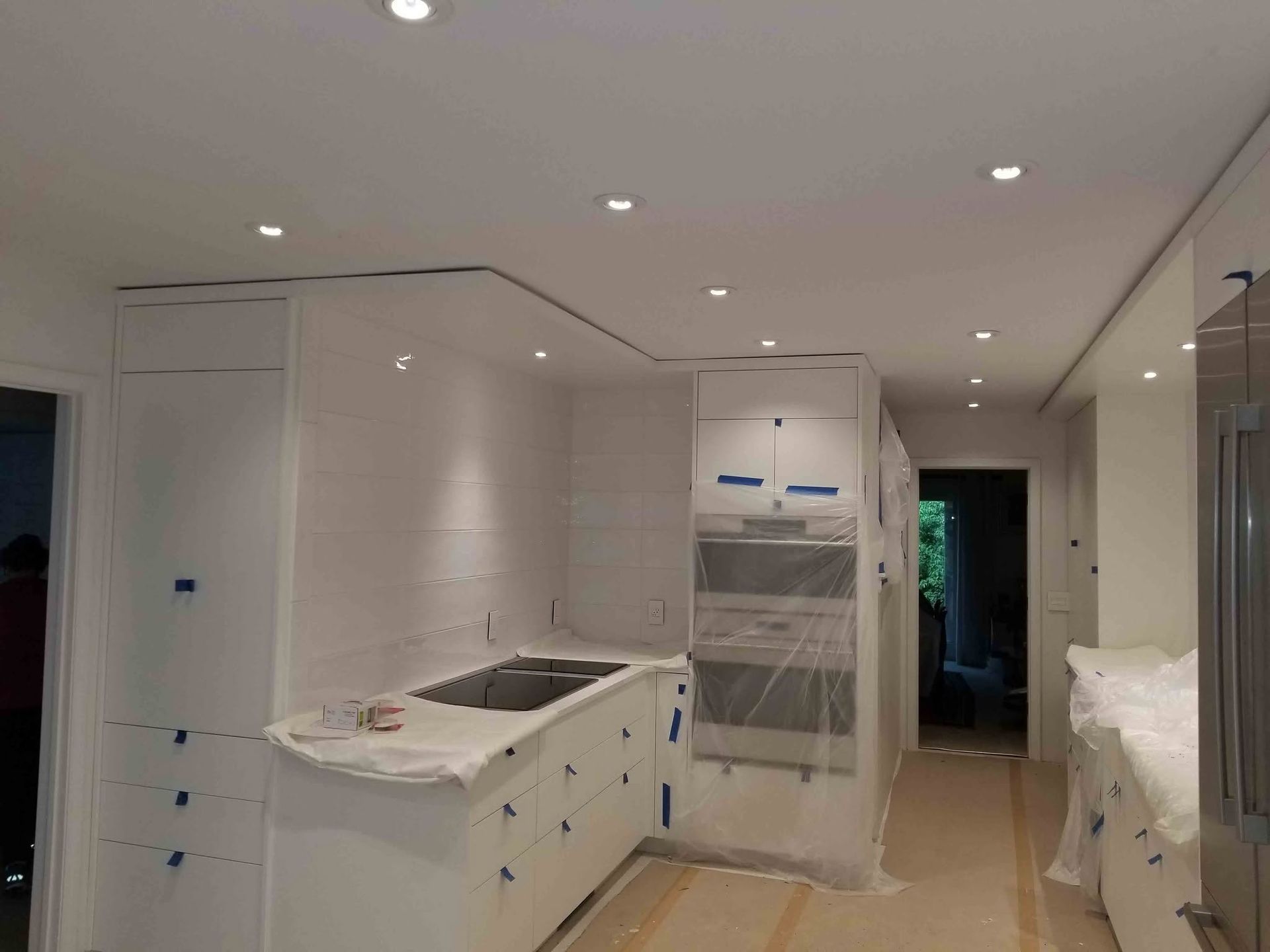 Bright white kitchen under renovation with cabinets, countertops, and built-in appliances installed