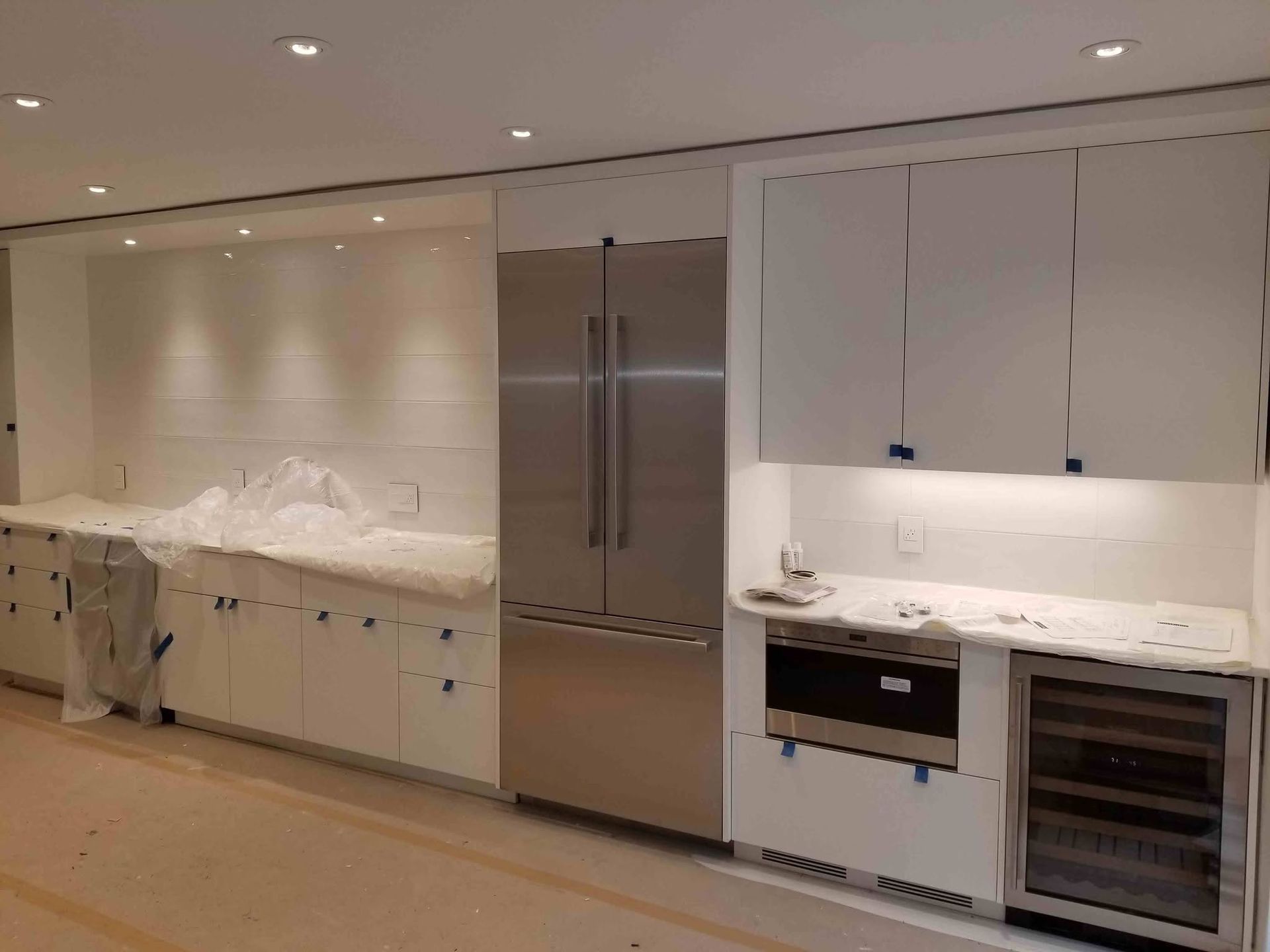 Modern white kitchen with marble countertops, stainless steel fridge, oven, and built-in cabinets