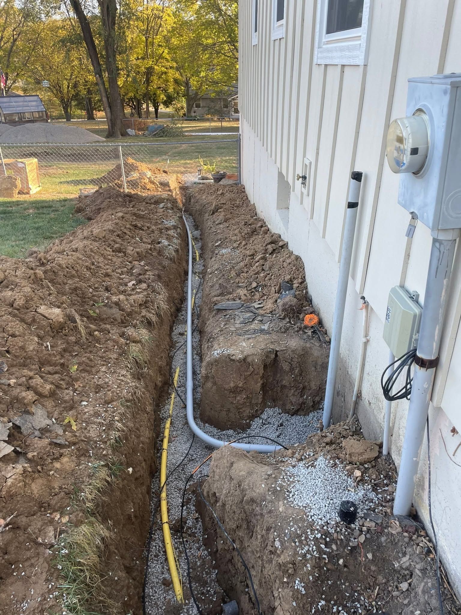Trench beside house with exposed conduit and electrical boxes during utility installation