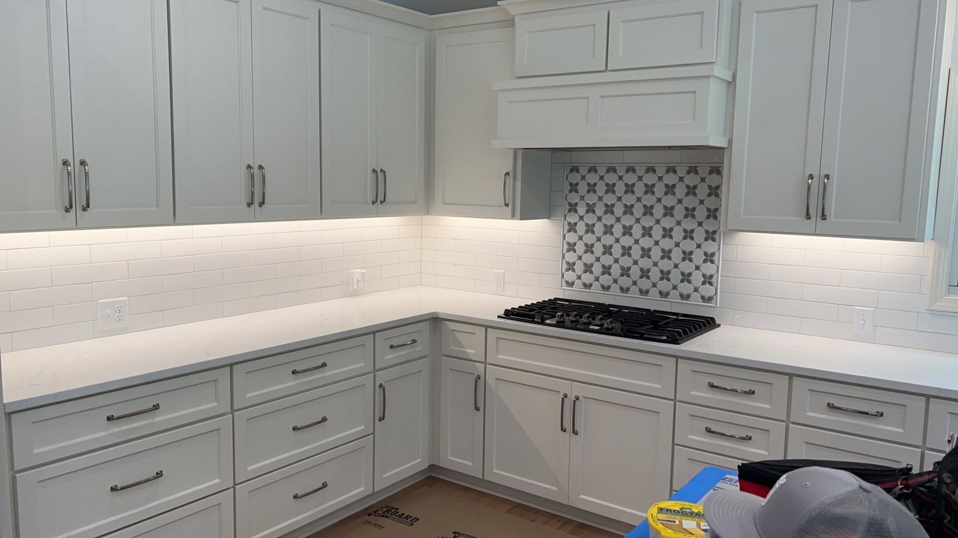 Bright white kitchen with gray cabinets, marble countertops, patterned backsplash, and gas range.