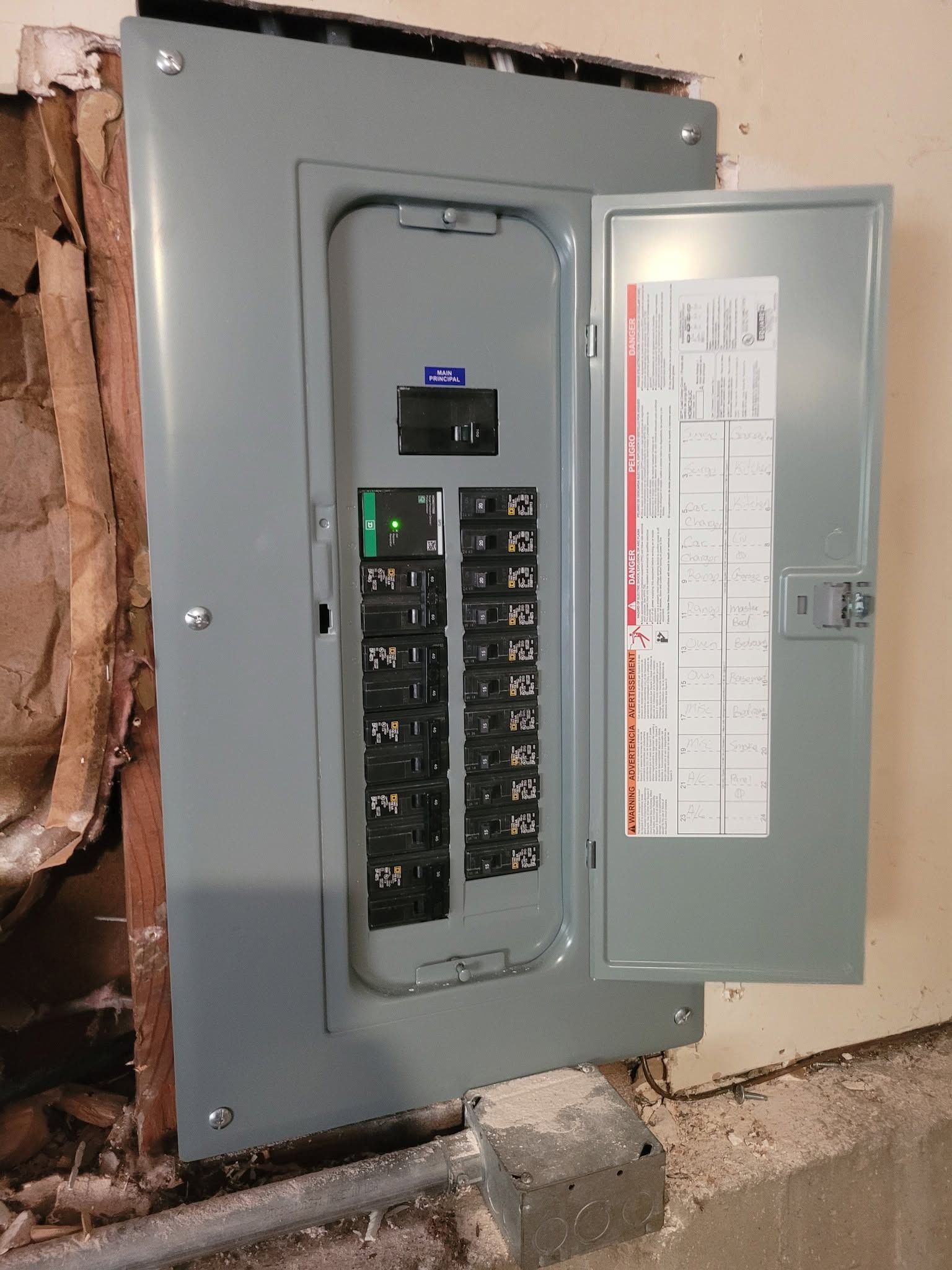 Open electrical breaker panel in a wall, with the circuit directory on the inside door.
