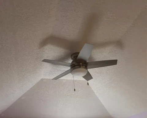 Ceiling fan with five blades on a textured white ceiling, viewed from below.