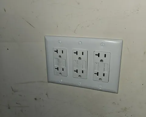 Three white electrical outlets on a white wall plate against a scuffed beige wall