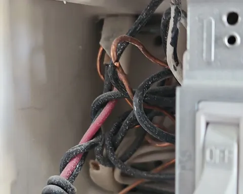 Close-up of tangled black and red electrical wires inside an open wall switch box
