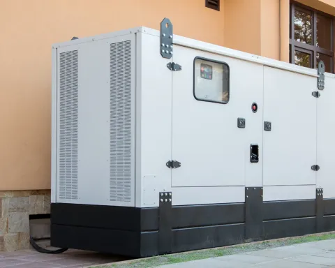 White industrial generator unit beside a building, with vents, doors, and black base.