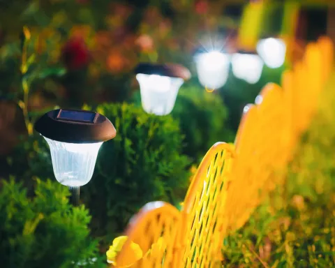 Glowing garden path lights among green shrubs with blurred warm lights in the background