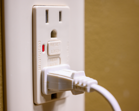 Electrical outlet with a plugged-in cord and built-in reset/test buttons on a wall plate.