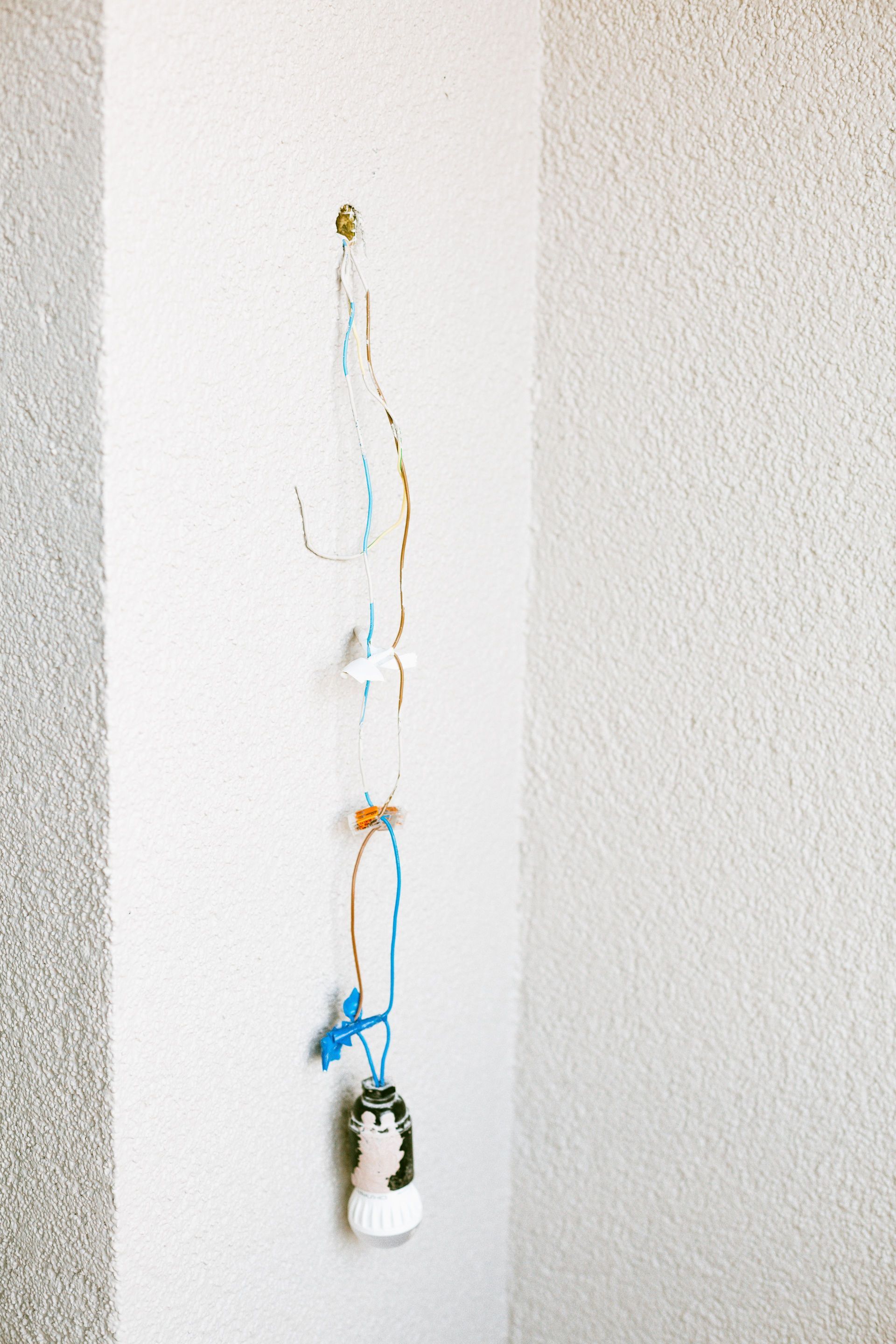 White wall with a dangling blue-orange cord and a small white device hanging near the bottom.