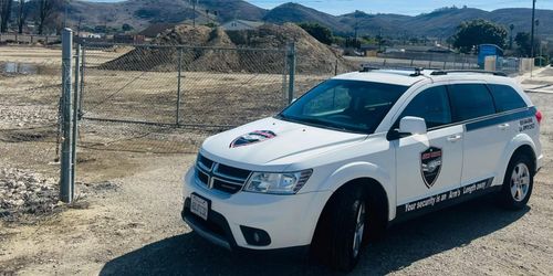A white suv is parked in a gravel lot next to a fence.