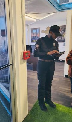 A security guard is standing in a room looking at a tablet.