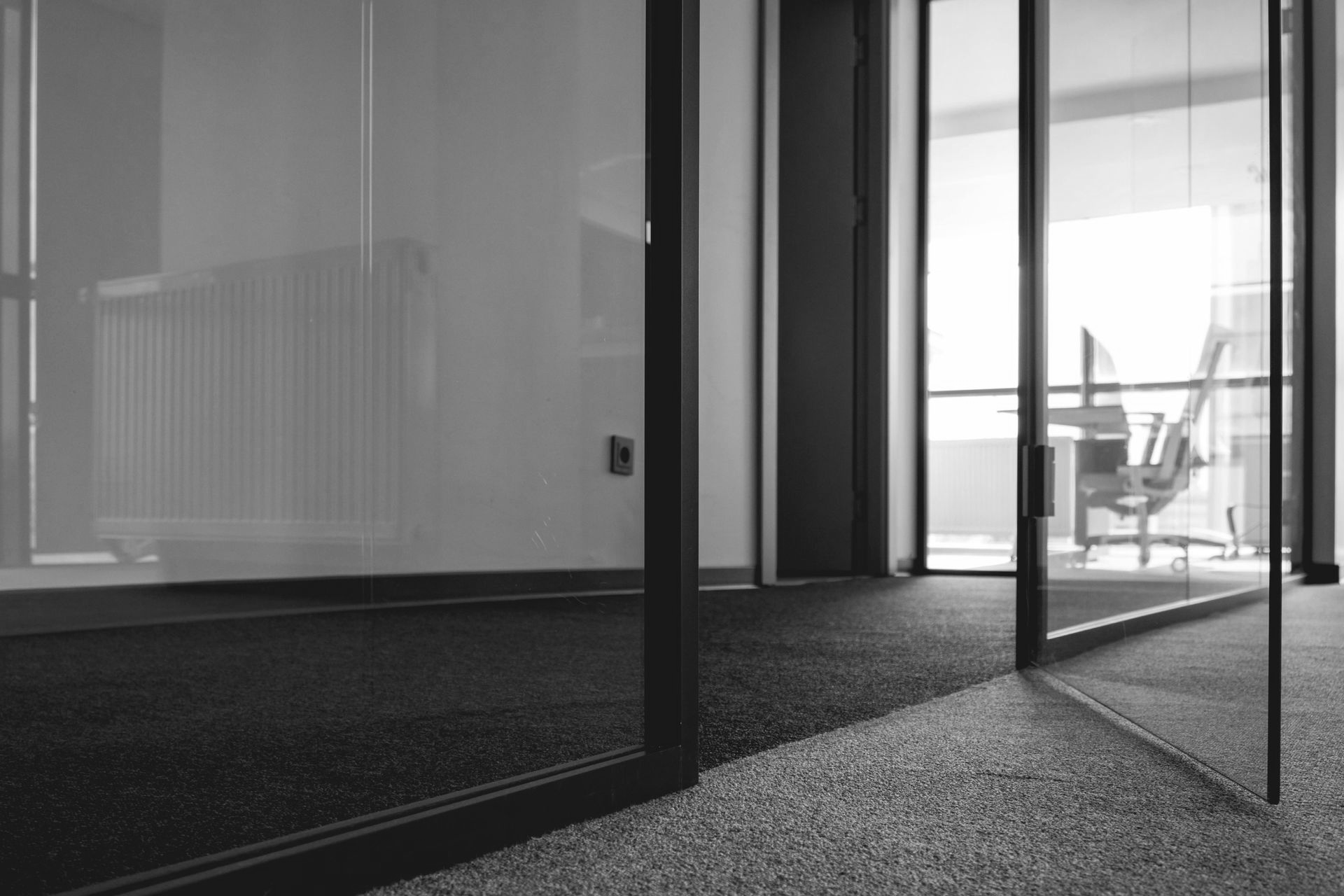 Glass office doors with dark frames, leading to a brightly lit office with furniture visible.