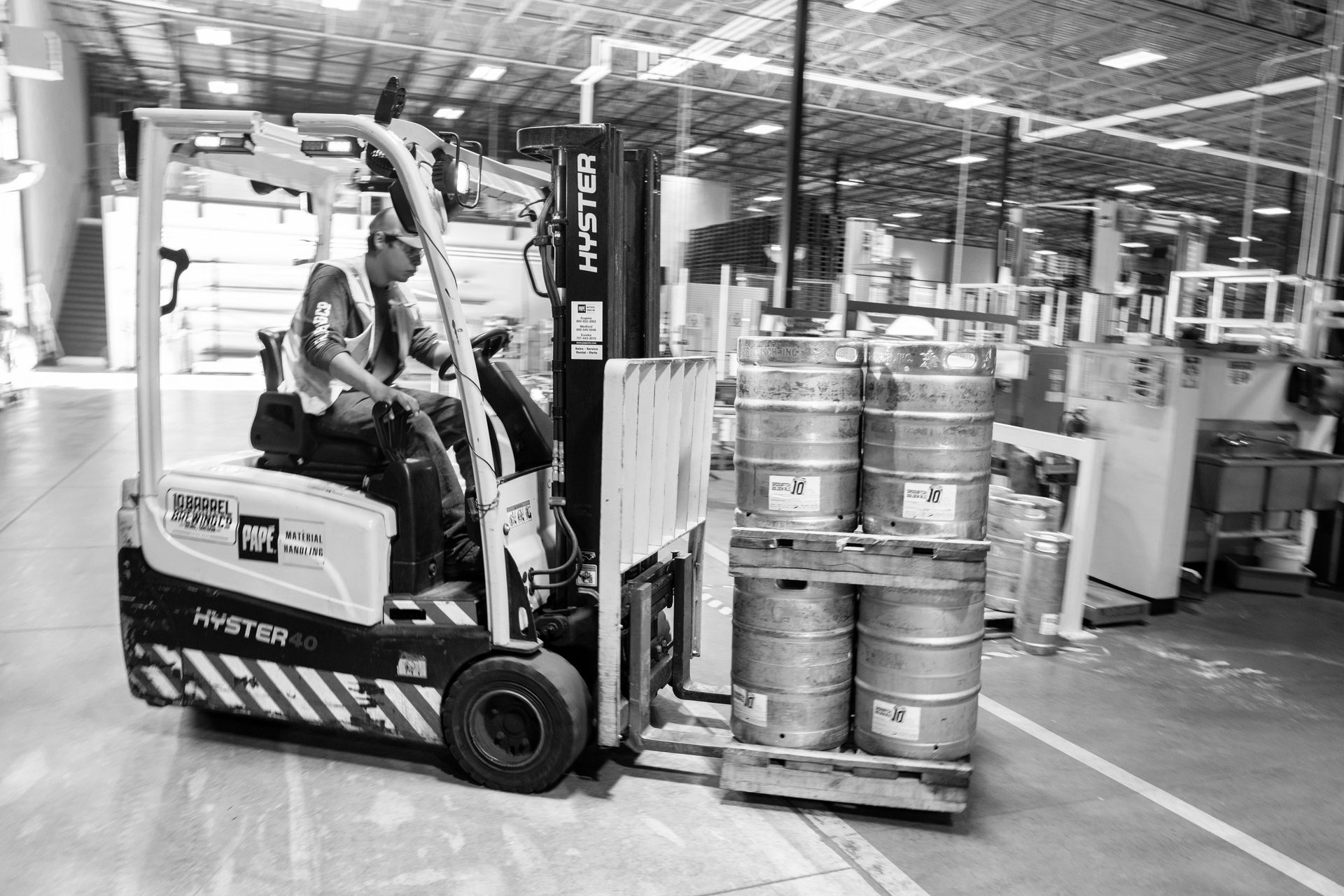 Forklift carrying kegs in a warehouse. Operator wears a vest.