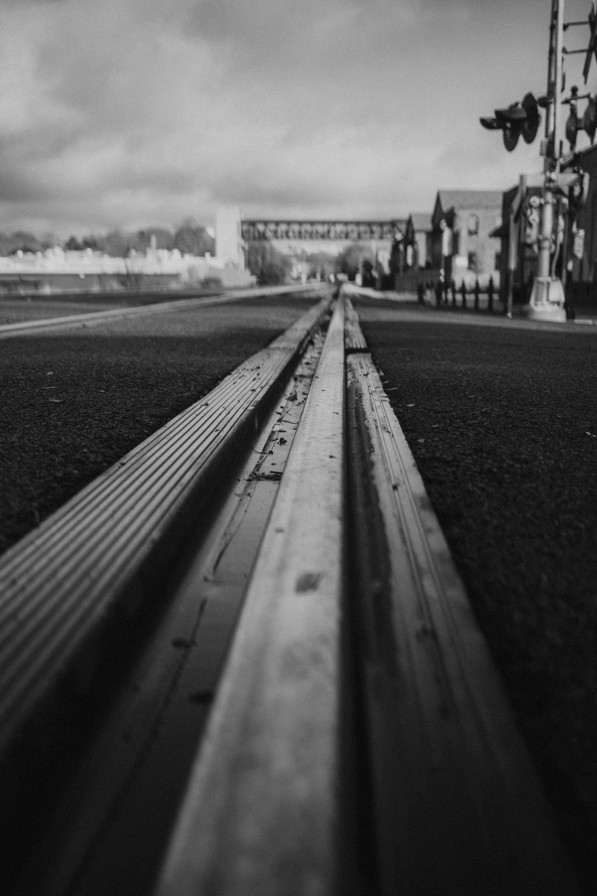 Black and white photo of train tracks receding into distance, leading towards urban buildings and a bridge.