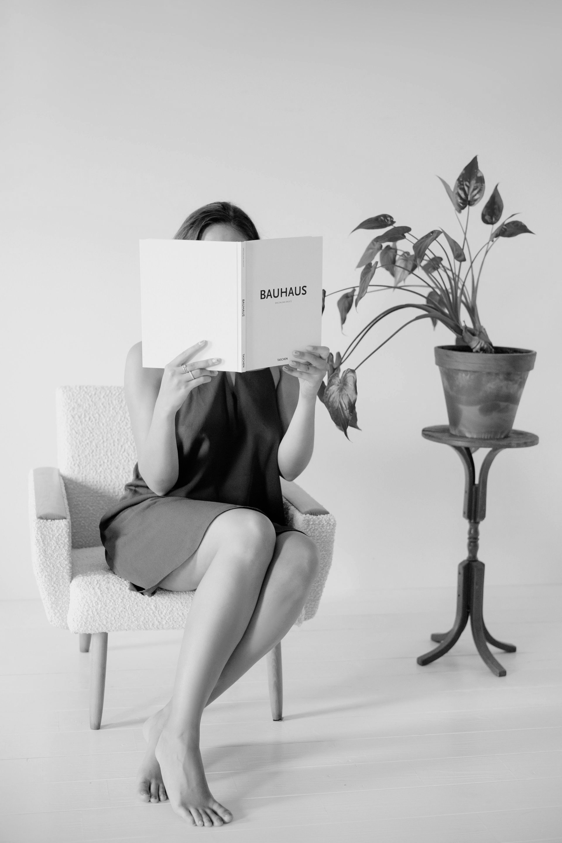 Woman in glasses in a chair, holding papers, talking to someone. Small table with notebook. Modern office setting.