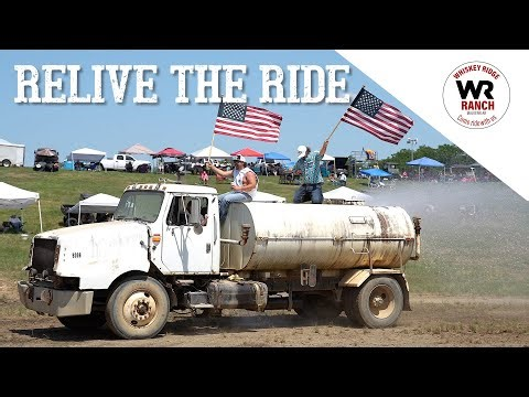Vintage white tanker truck driving through mud with spectators waving flags in the background