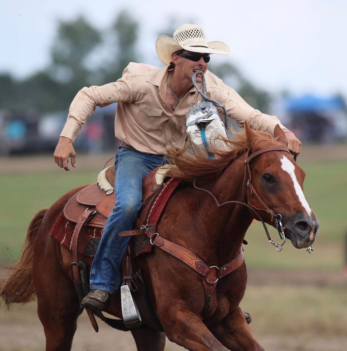 Cowboy riding a brown horse at a rodeo, leaning forward as the horse runs.