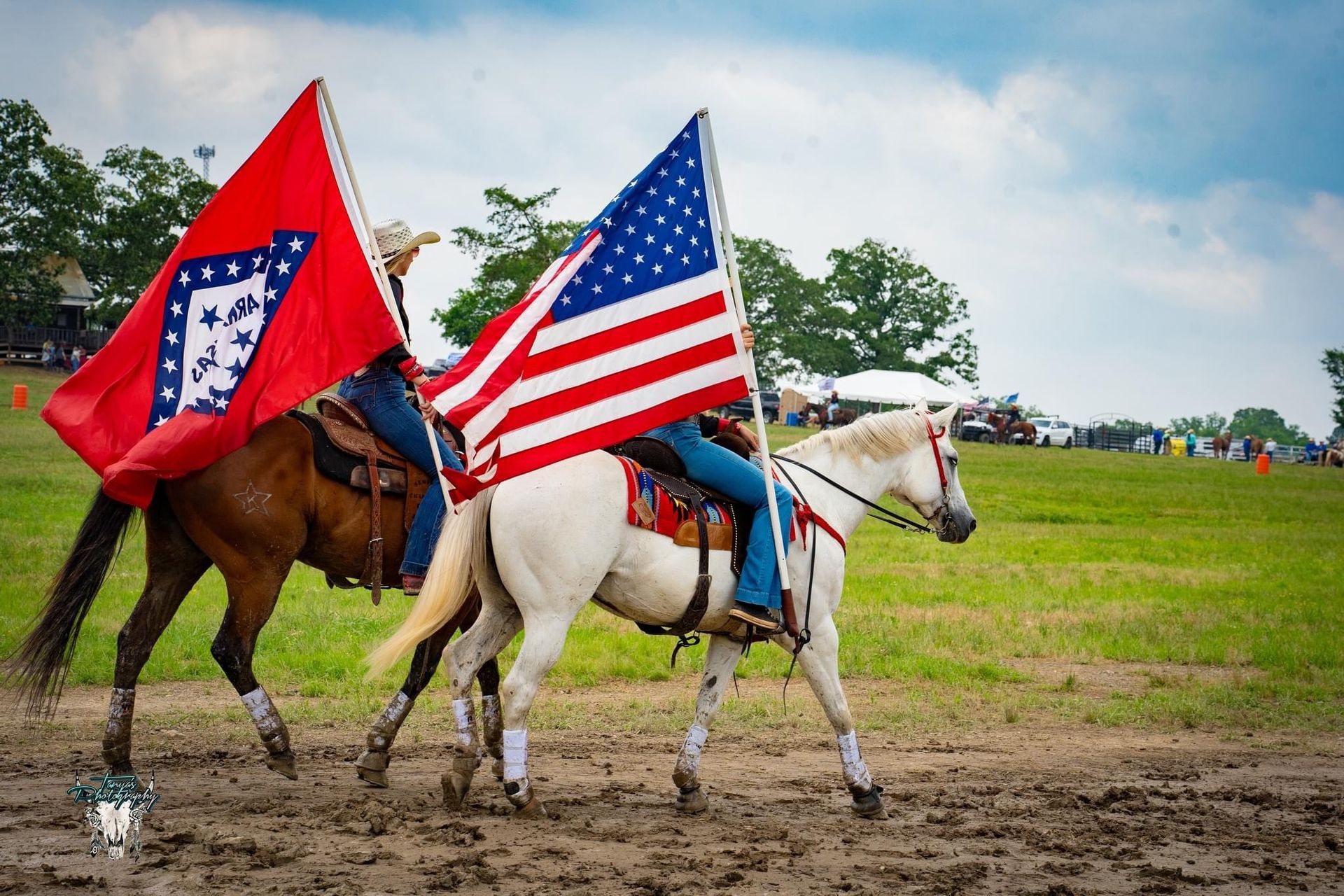 Two riders on horseback carrying American and Arkansas flags in a muddy field
