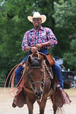 Person in cowboy hat riding a brown horse at an outdoor event