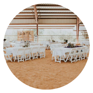Rustic event hall with white tables and chairs under a wooden-roofed pavilion