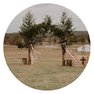 Two decorated trees forming an outdoor wedding arch in a grassy field
