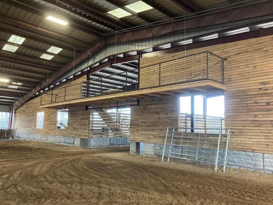 Indoor equestrian arena with dirt floor, wooden walls, and a raised viewing platform