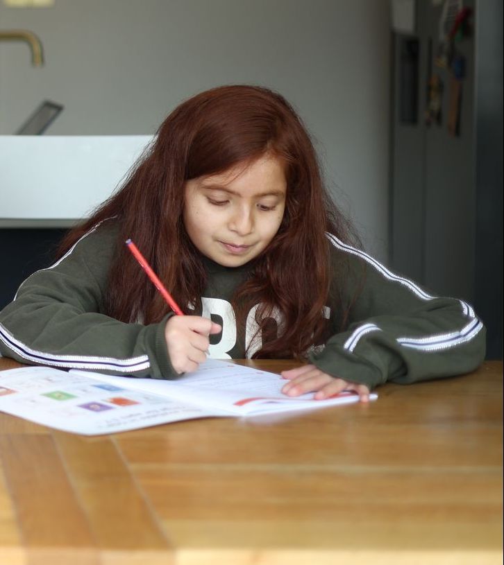 A young girl is sitting at a table writing in a notebook