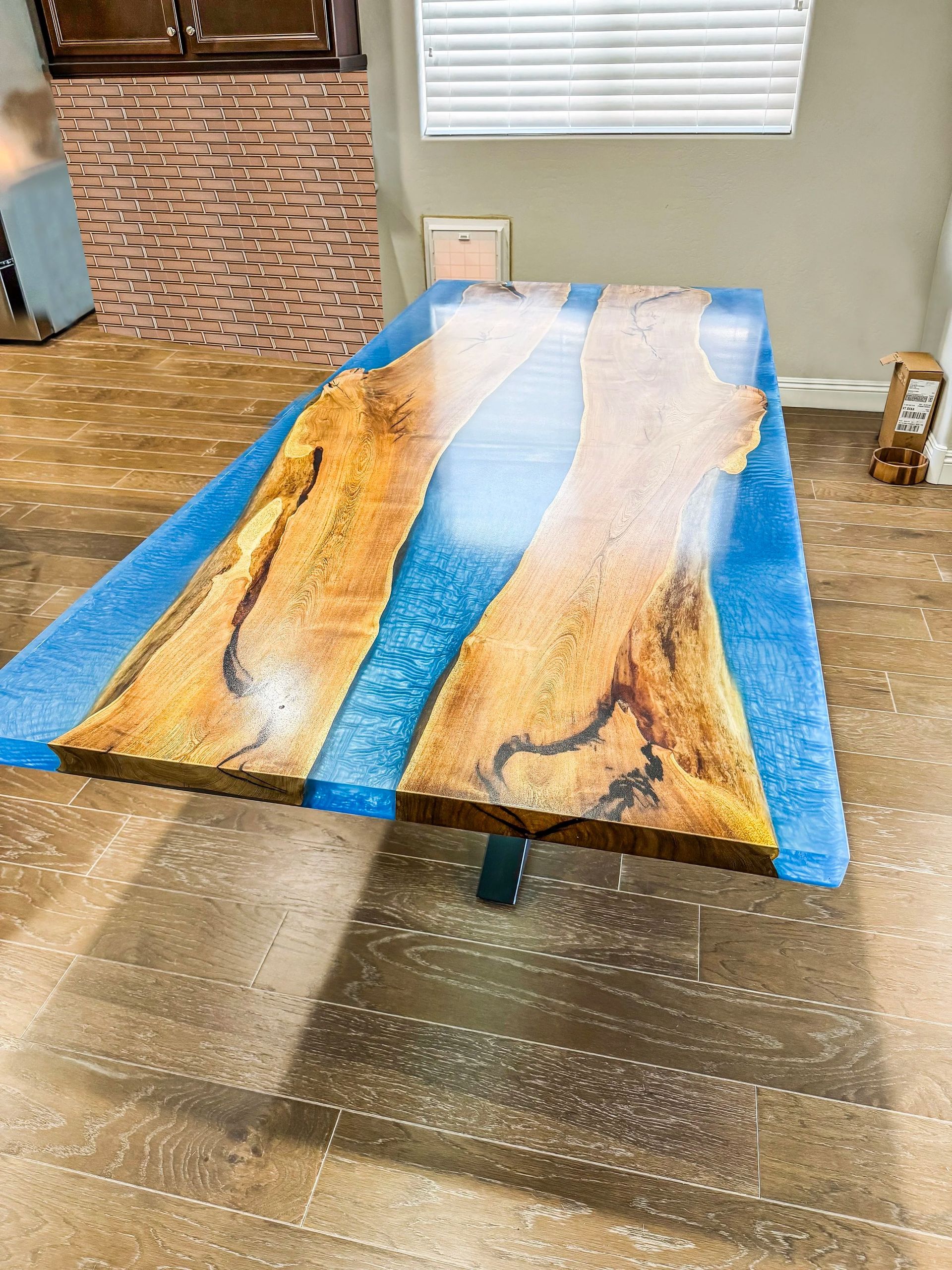 A live-edge wood table with blue resin river in a room with wood flooring.