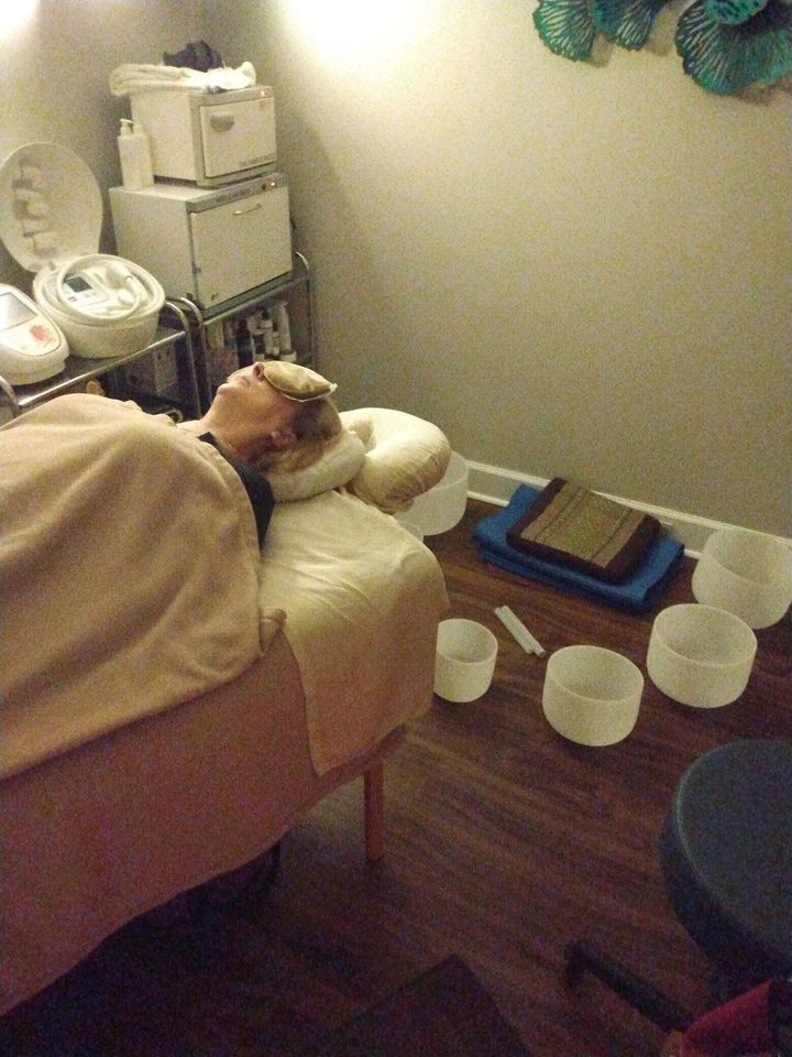 Person reclining in a massage chair with bowls and folded towels on the floor in a spa room