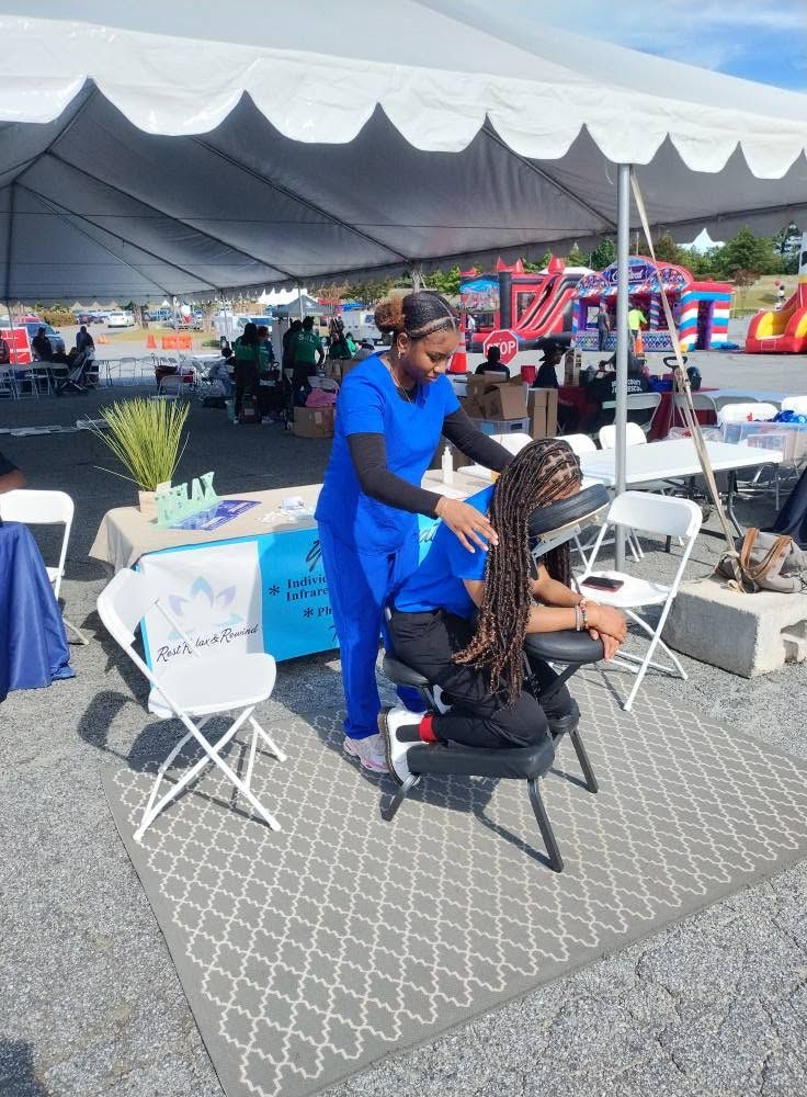 Braider styling hair in a blue dress at an outdoor fair under a large white tent
