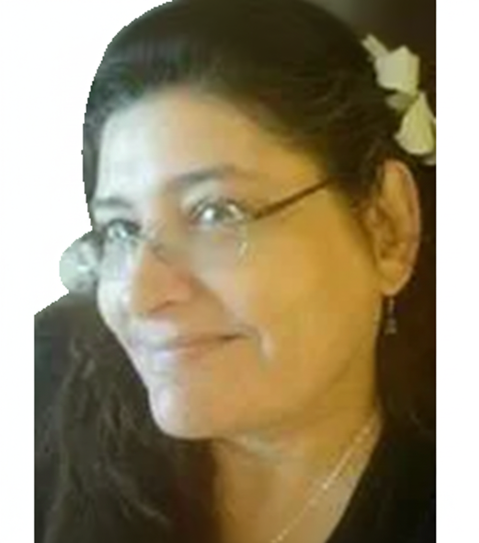 Woman with glasses smiling in profile, wearing a dark top and white flower hair clip.
