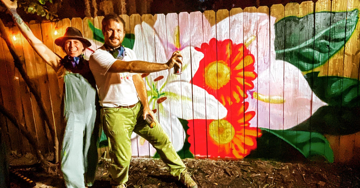 Mural created live as a painting performance for the Real 904 real estate event in St. Augustine, Florida. The spray painting features a large lily and tropical flowers. Ian and Danielle of Heartspace Art stand pose in frond of the painting at the end of the event.