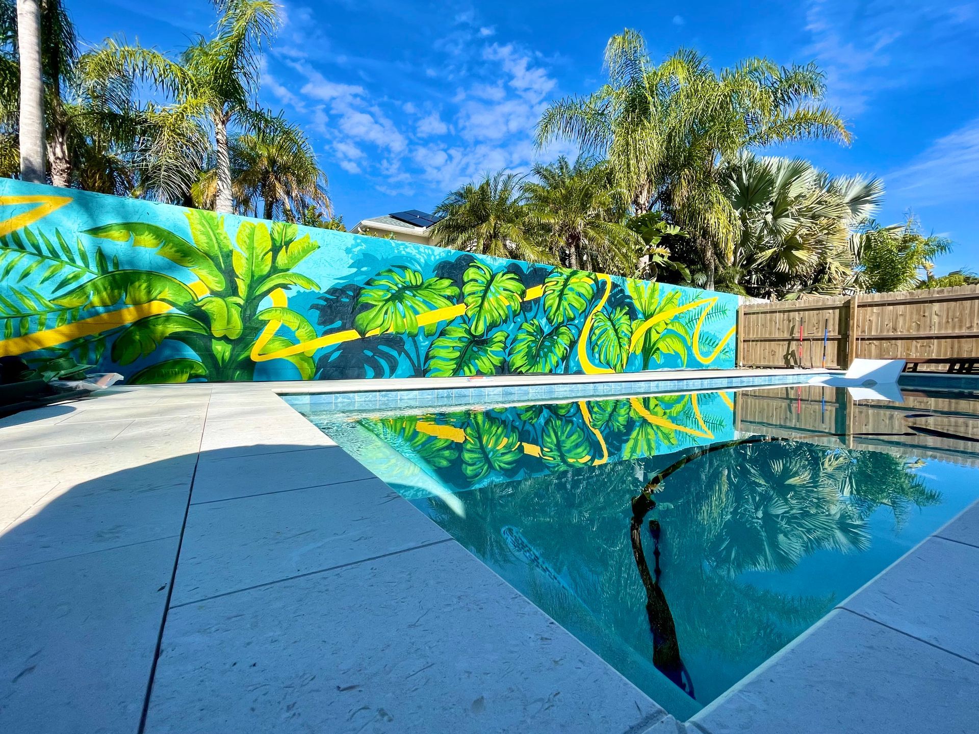 This pool side mural/wall art was spray painted in a graffiti art style for an Airbnb short term rental in Vilano Beach, St. Augustine, Florida. The mural features vibrant and deep blues as well as Monstera, Banana, Palm leaves, and artistic yellow line that creates unity across the piece.
