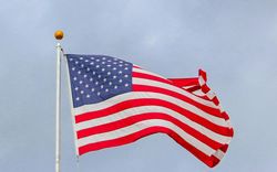 The United States flag flying on a pole against a light blue, overcast sky.
