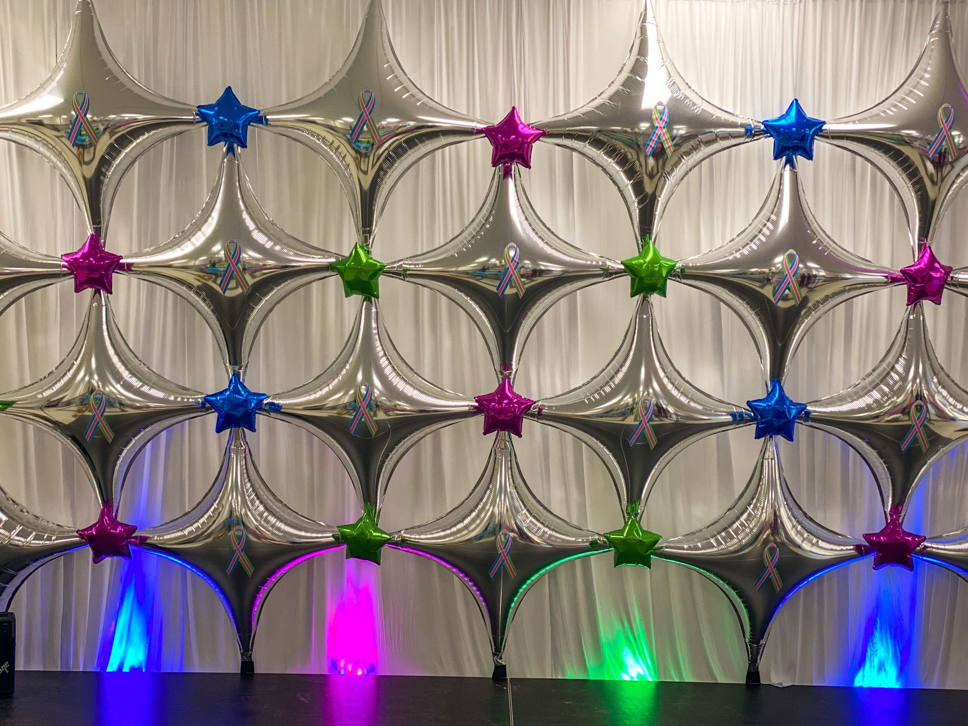A wall made of balloons and stars with lights behind it.