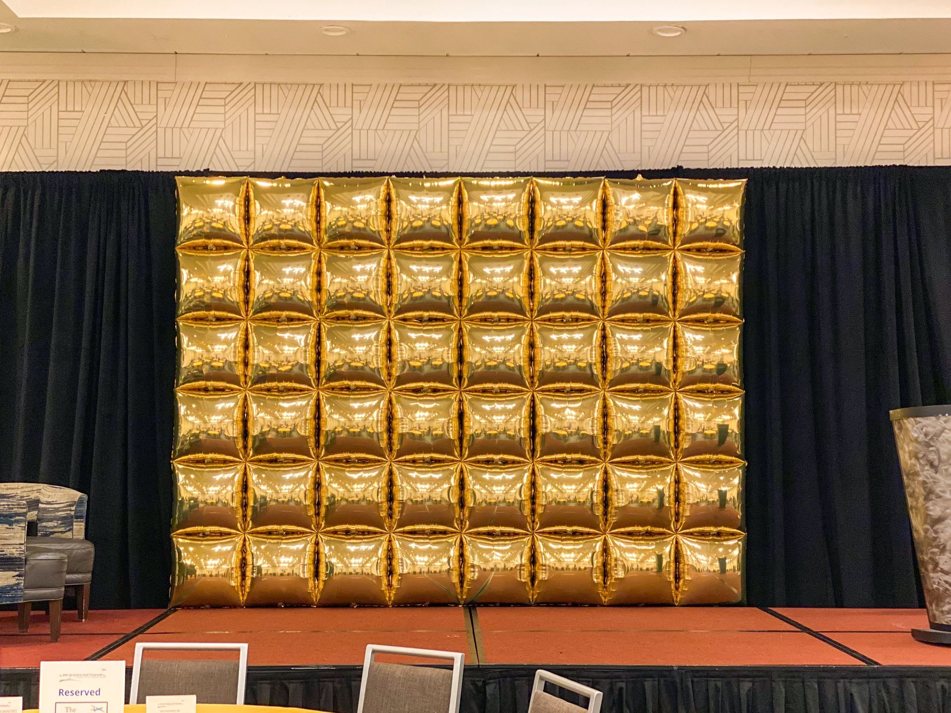 A stage with a wall of gold balloons on it.