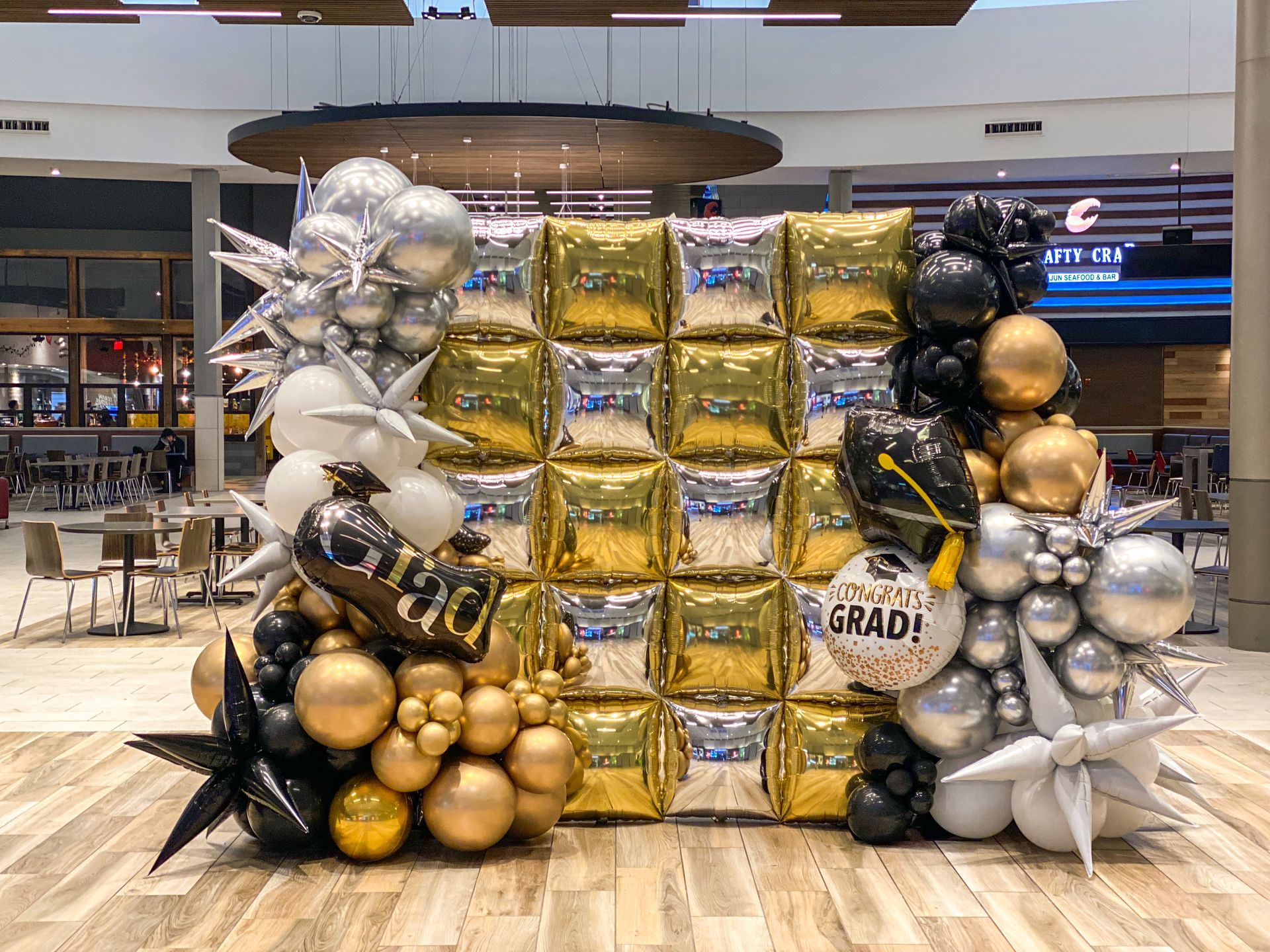 A bunch of balloons are sitting on a wooden floor in a mall.
