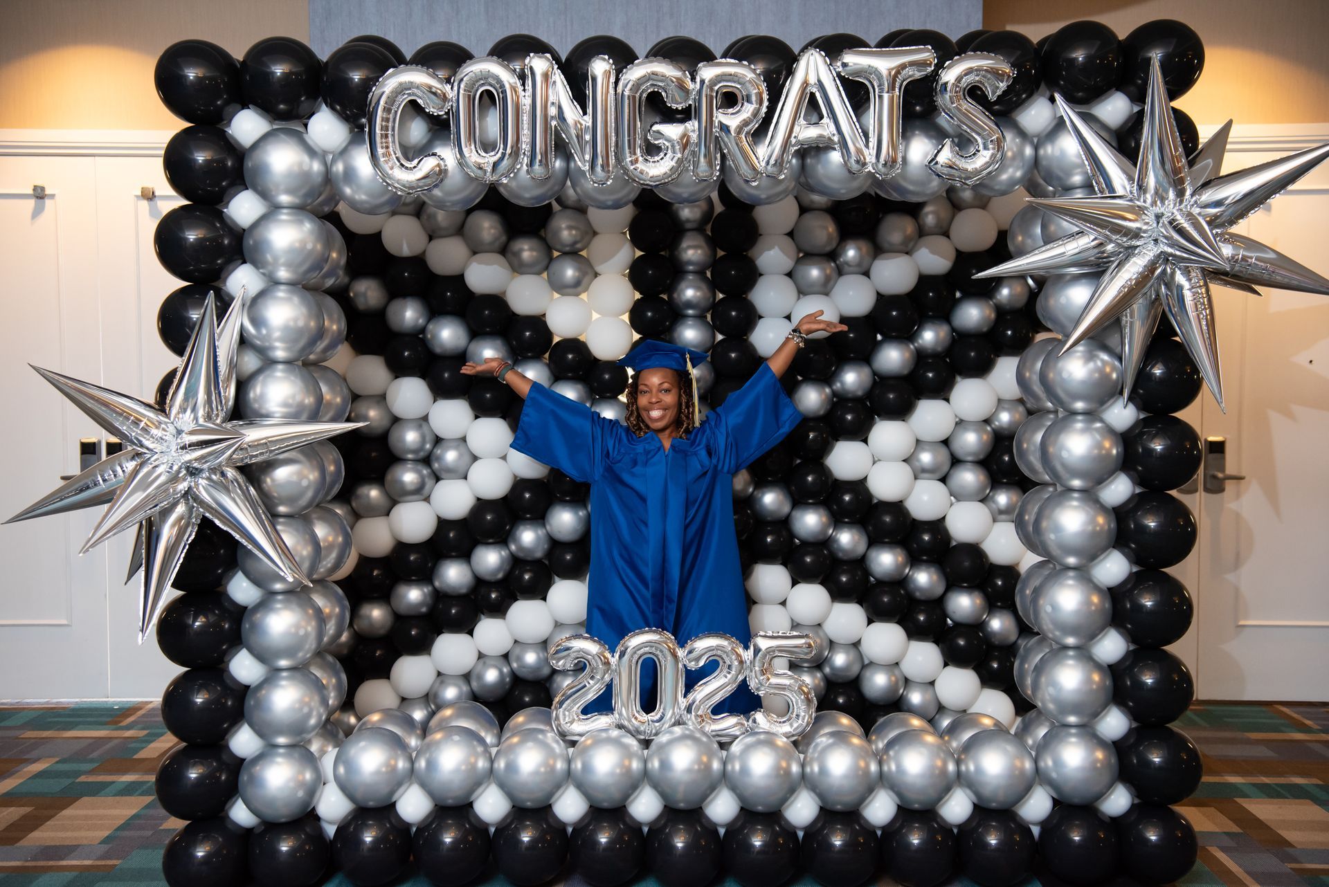 A graduate is standing in front of a wall of balloons.