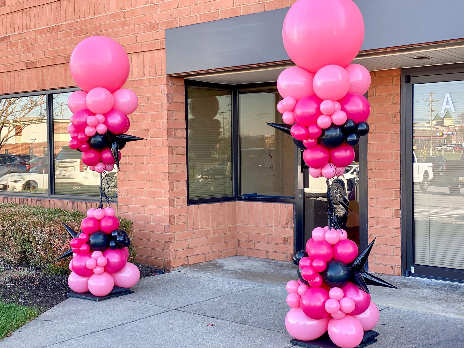 Two pink and black balloon columns are sitting in front of a brick building.